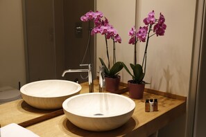 A bathroom with two large, round, beige sinks, a modern faucet, and two potted orchids.