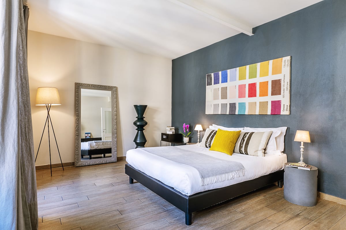 Un dormitorio moderno con una cama grande, una paleta de colores en la pared, un espejo, una lámpara y una mesita de noche.