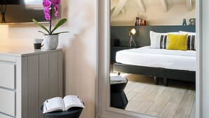 A bedroom with a large mirror reflecting the room, a bed with white bedding, a bedside table with a book, and a potted plant. - Residenza dell'Opera (Turin)