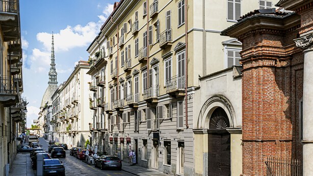 A street lined with multi-story buildings, featuring balconies and a prominent tower in the background. - Residenza dell'Opera (Turin)