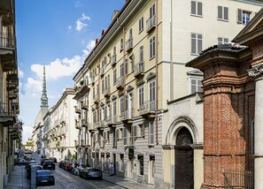 A street lined with multi-story buildings, featuring balconies and a prominent tower in the background. - Residenza dell'Opera (Turin)