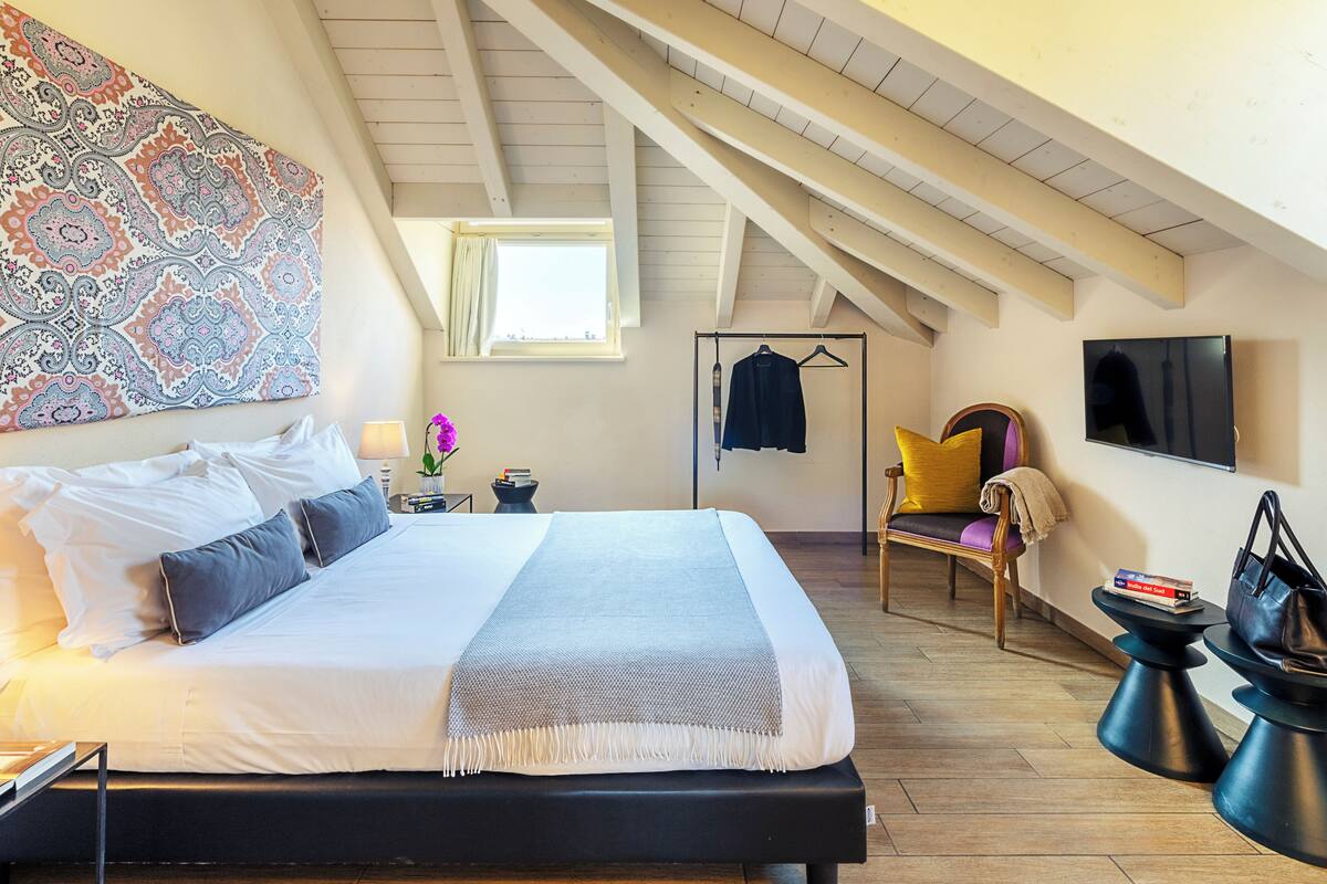 Un dormitorio con una cama grande, una silla colgante, un televisor y un papel tapiz estampado.