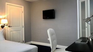 A hotel room with a bed, a desk with a laptop, a chair, a TV on the wall, and a lamp. - Ivoire Guest House (Sekondi-Takoradi)