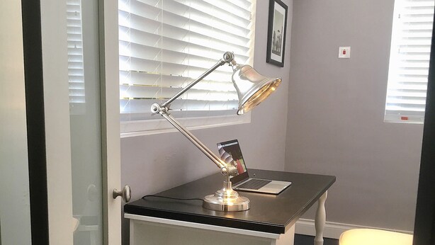 A small office space with a desk, chair, and a standing lamp. There is a trash can and a window with blinds. - Ivoire Guest House (Sekondi-Takoradi)