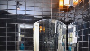 A bathroom with black tiled walls, a white sink, and a mirror. - Ivoire Guest House (Sekondi-Takoradi)