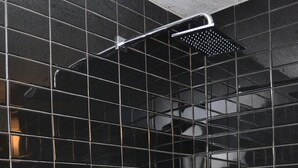 A shower area with black tiled walls and a chrome showerhead. - Ivoire Guest House (Sekondi-Takoradi)