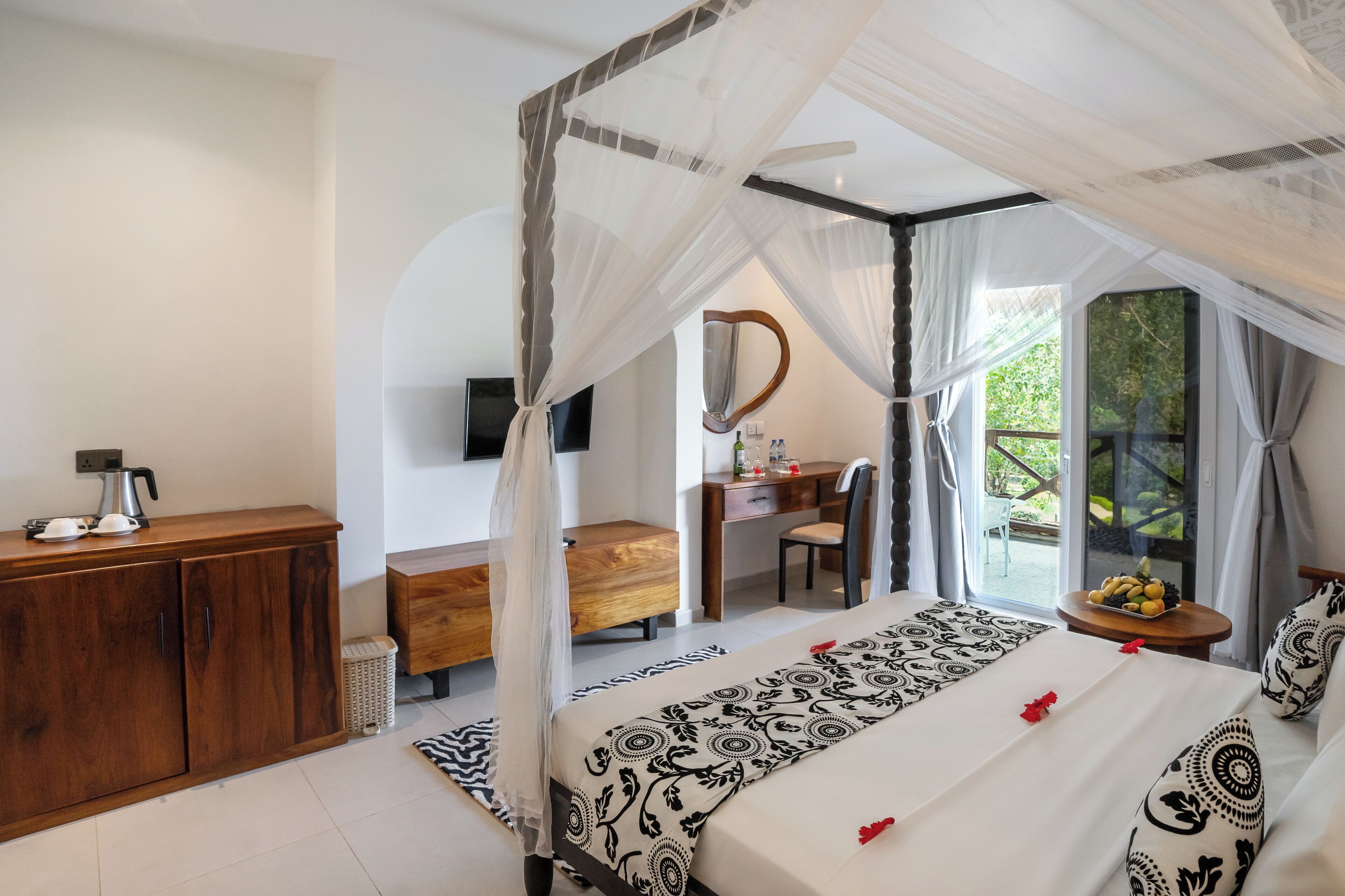 Ein Schlafzimmer mit einem Himmelsbett, einem Schreibtisch, einem Sessel und einem kleinen Tisch mit Obst.