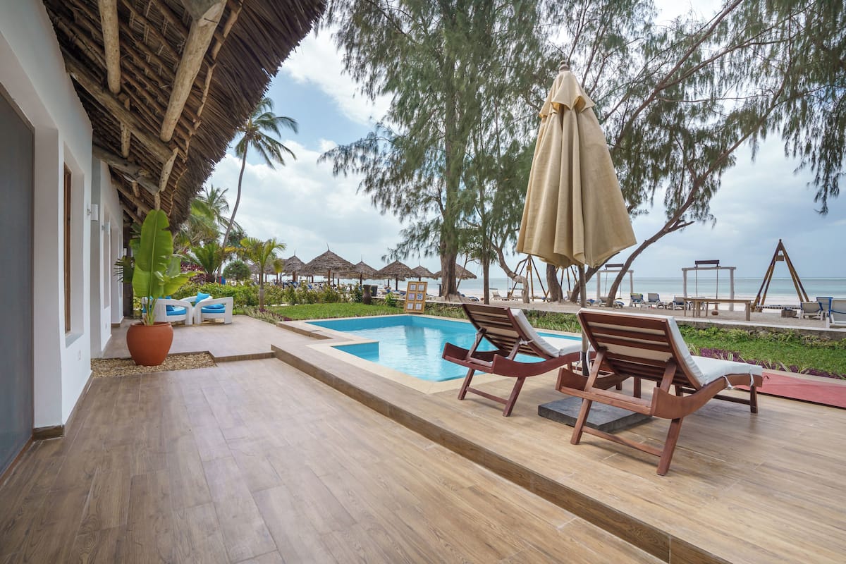 Un área junto a la piscina con sillones de madera, techo de paja y vista a la playa.