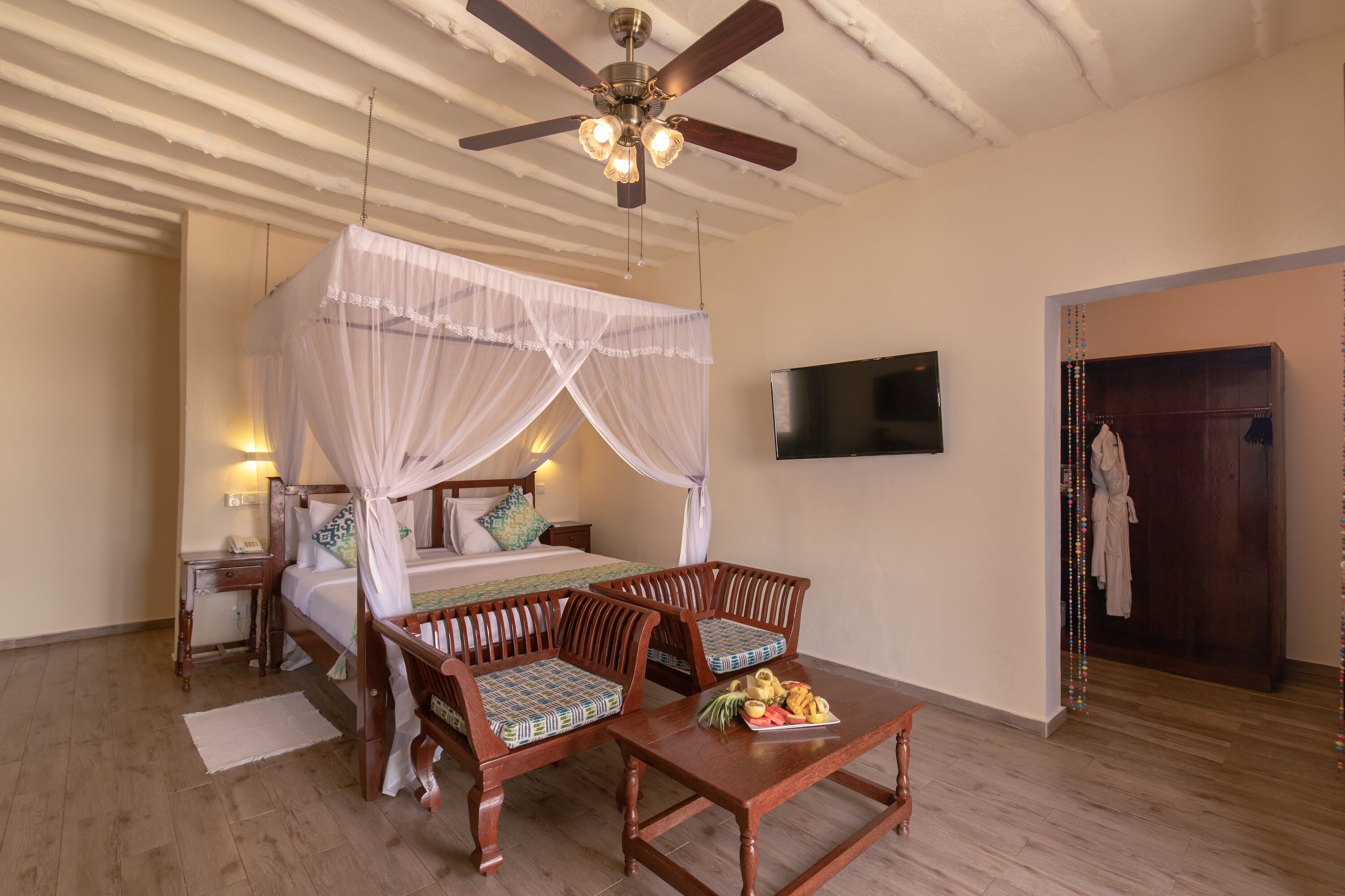 A bedroom with a bed, two wooden chairs, a bedside table, a TV, and a ceiling fan.