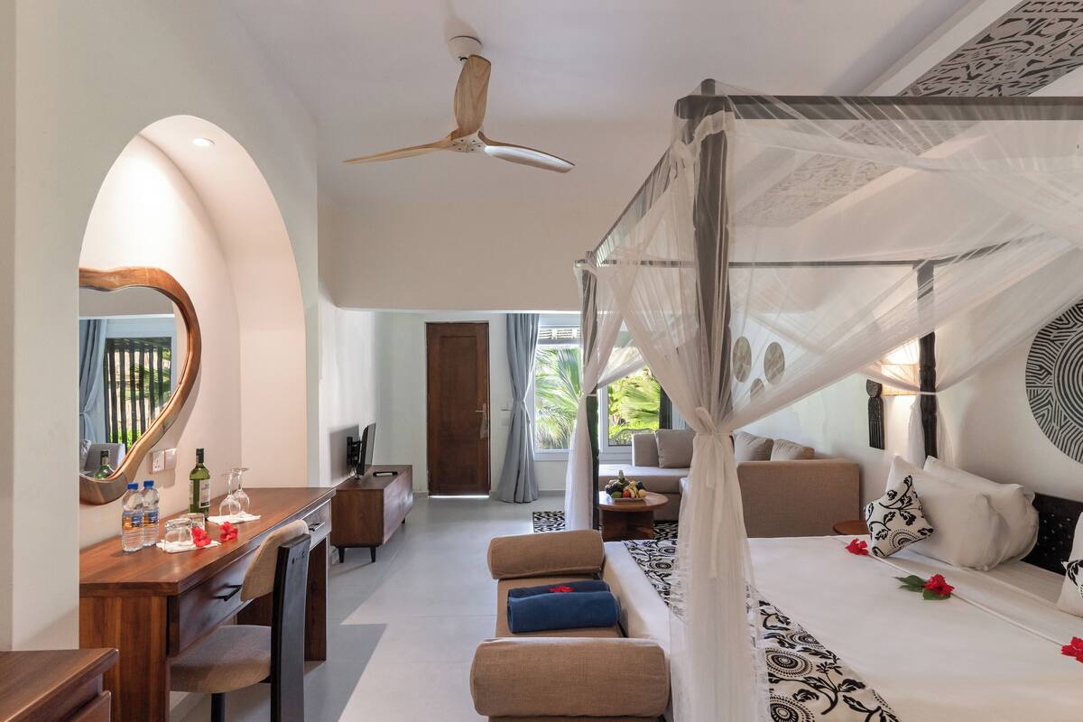 Habitación de hotel moderna con una cama grande, una zona de estar, un escritorio y un ventilador de techo.