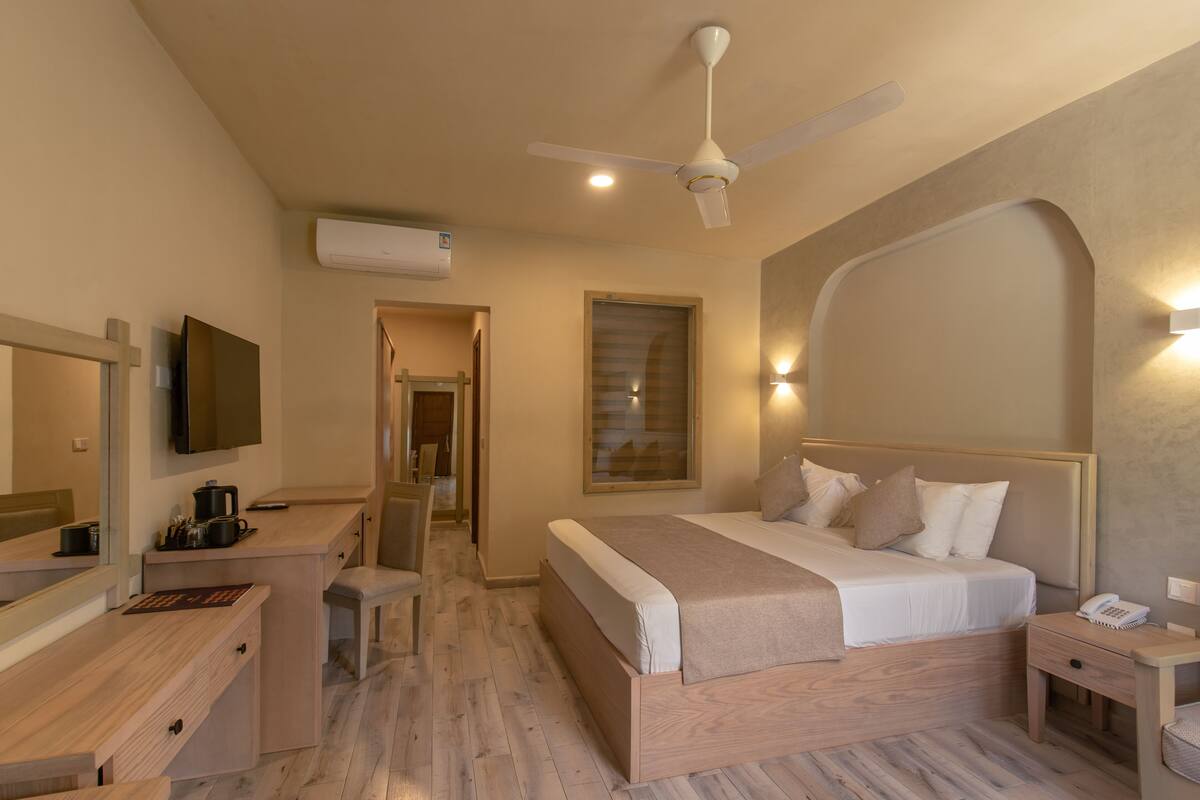 Una habitación de hotel con cama, mesita de noche, escritorio, silla y ventilador de techo.