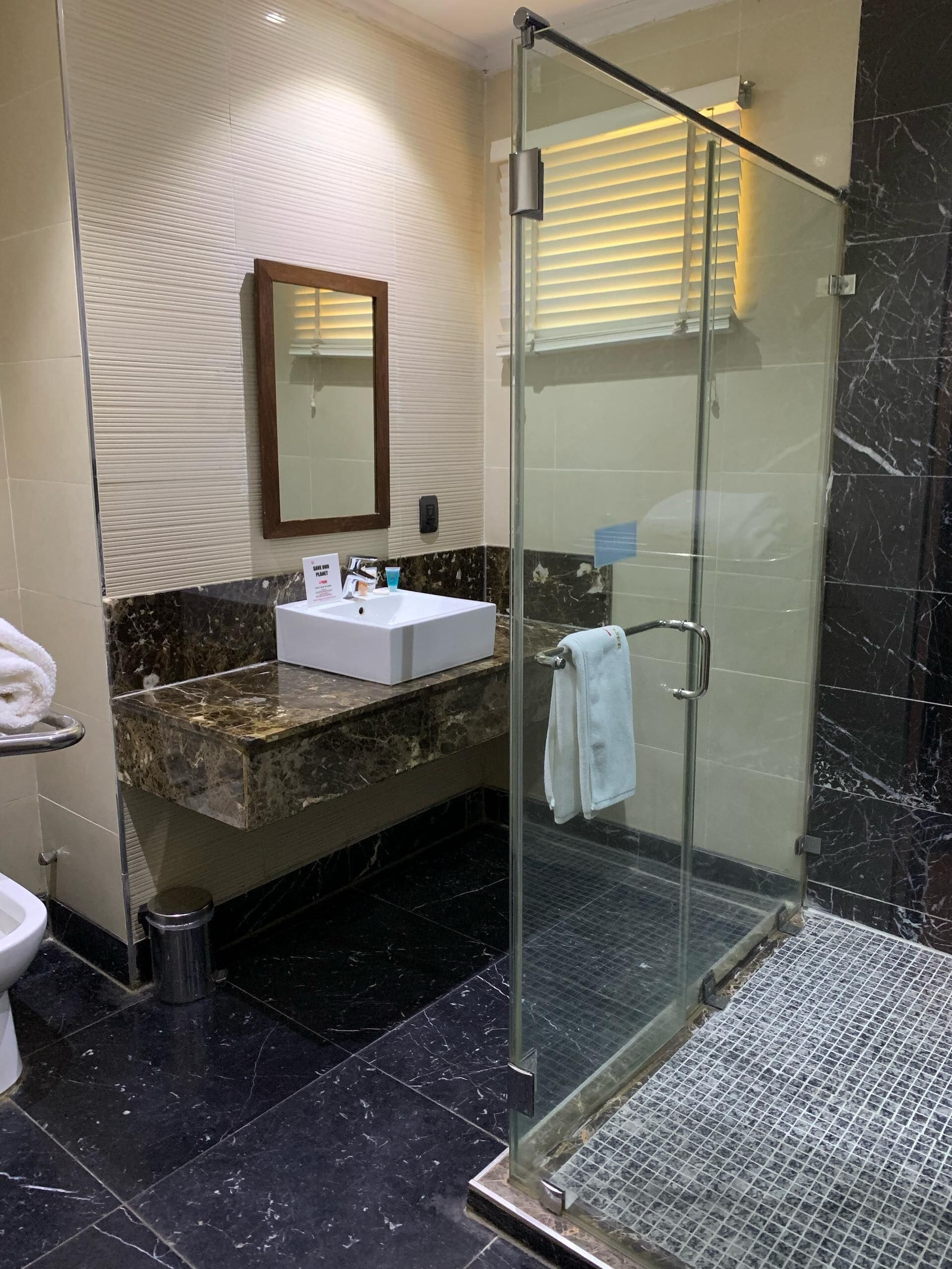 A modern bathroom with a glass-enclosed shower, a marble countertop sink, and a large mirror.