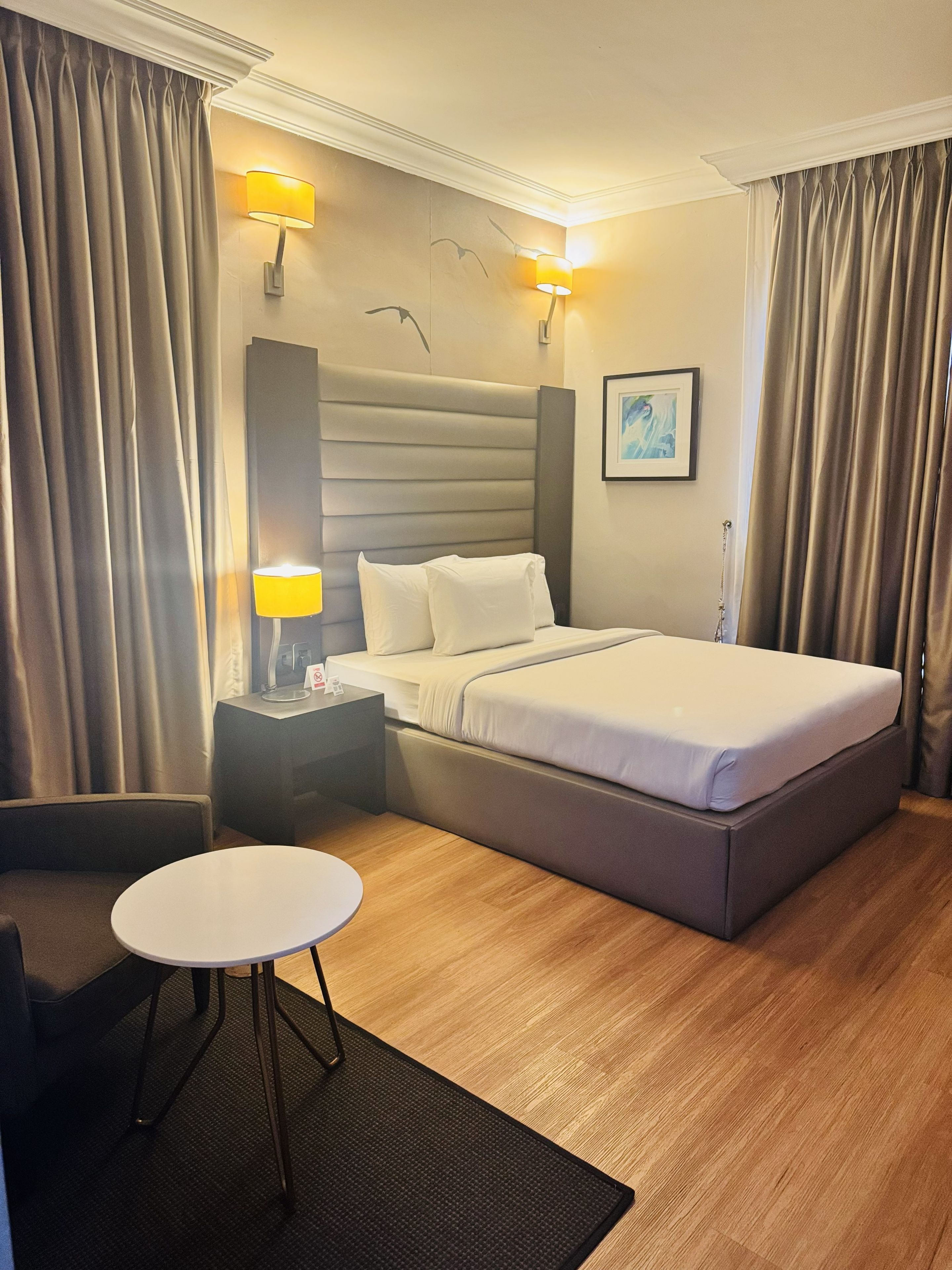 Una habitación de hotel con cama, mesitas de noche, un escritorio, una silla y una mesa redonda.
