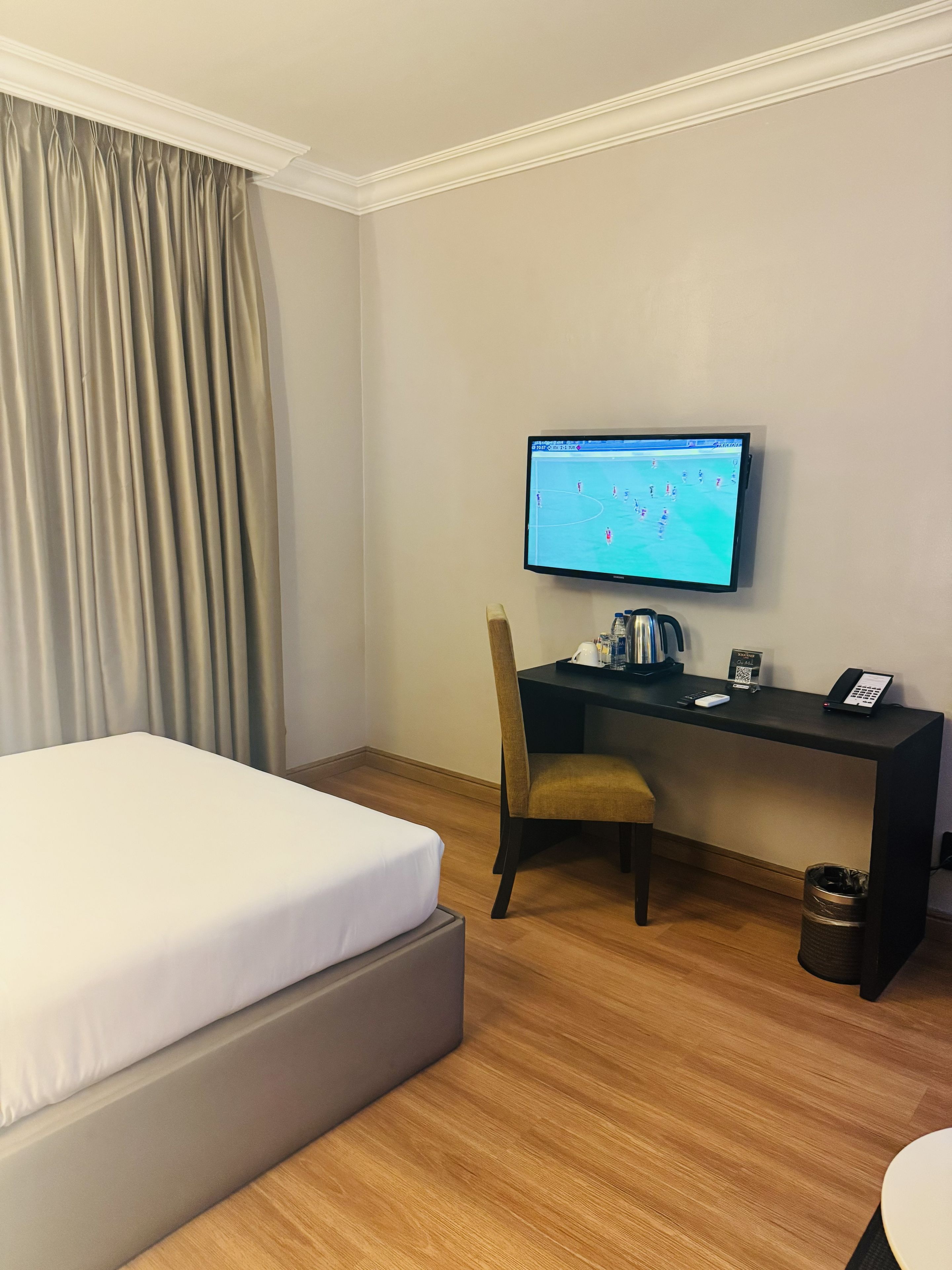 A hotel room with a bed, a desk with a computer, a chair, and a trash bin.
