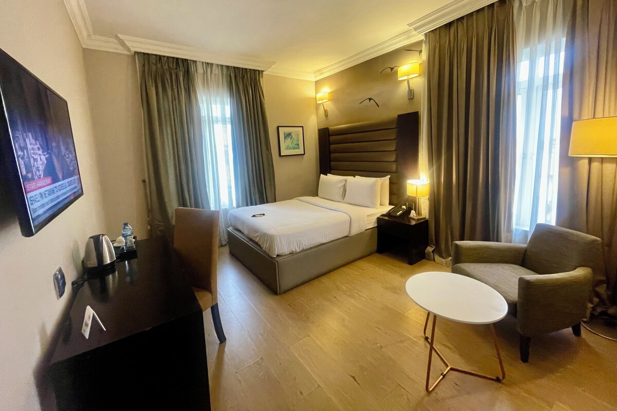 A hotel room with a bed, bedside table, chair, desk, and a TV.