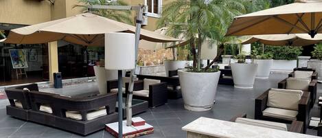 An outdoor seating area with wicker furniture, large umbrellas, and potted plants.