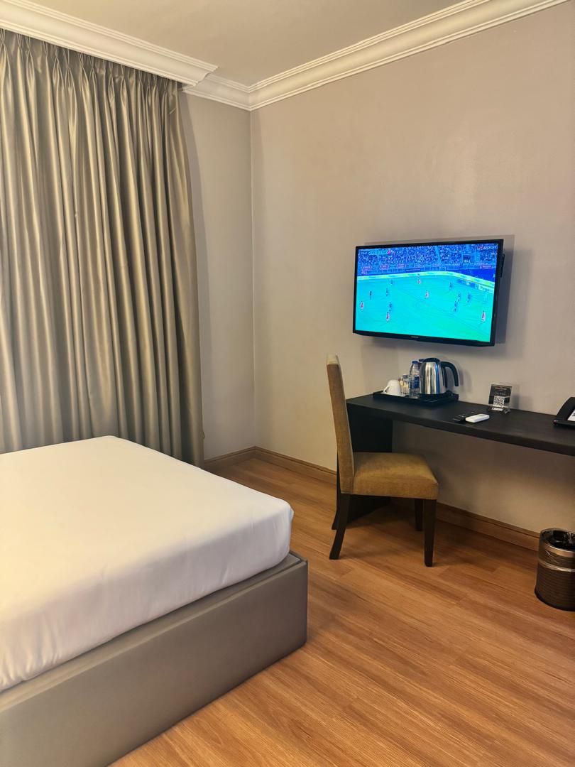 Habitación de hotel con cama, escritorio, silla, televisor y cafetera.