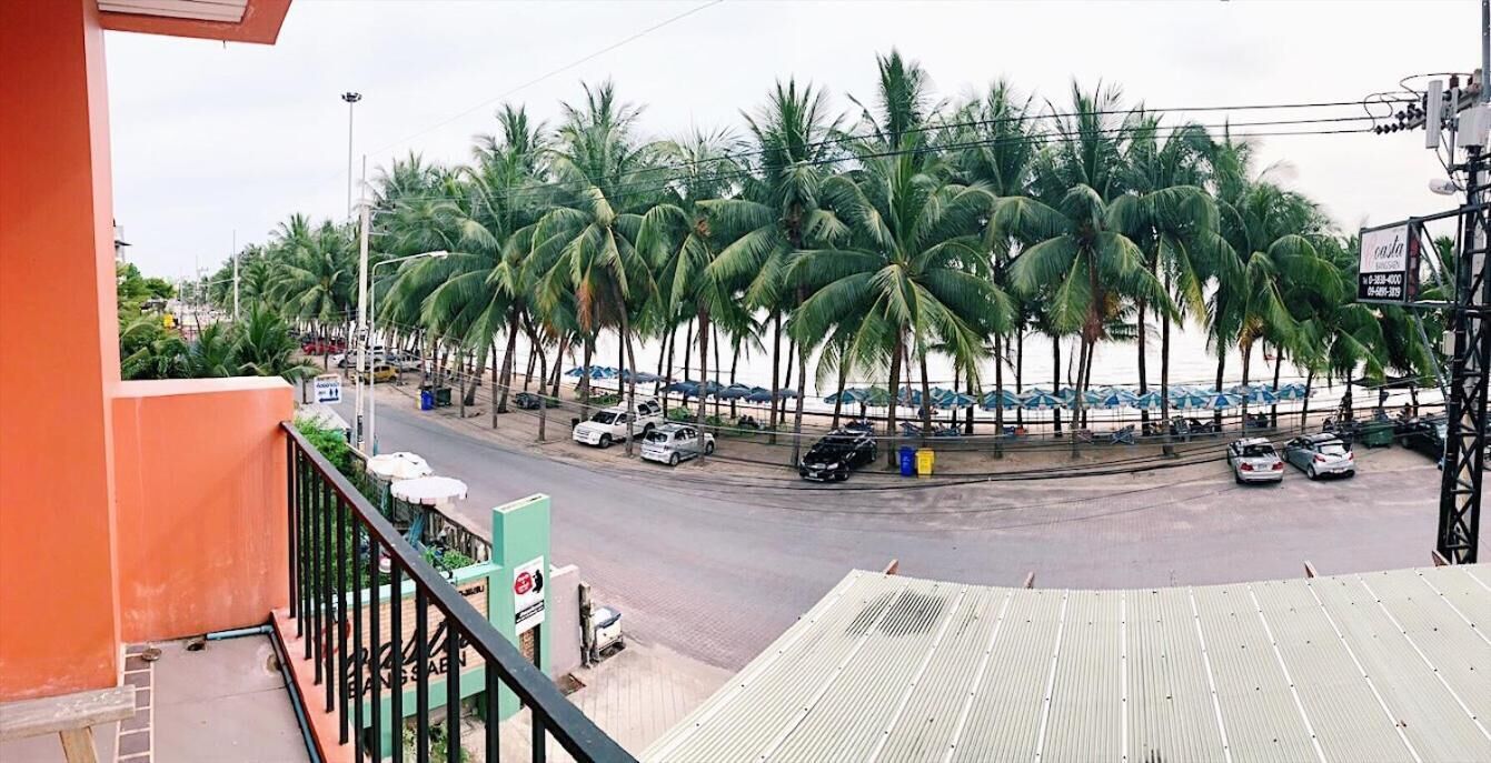 A street view with palm trees, parked cars, and a building with a balcony.