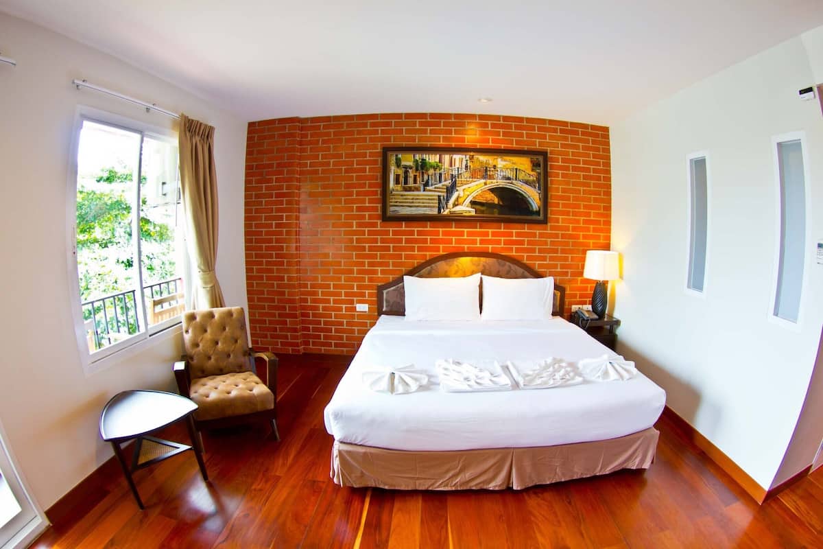 Habitación de hotel con cama, una silla, ventana con vistas y un cuadro en la pared, además de una lámpara.