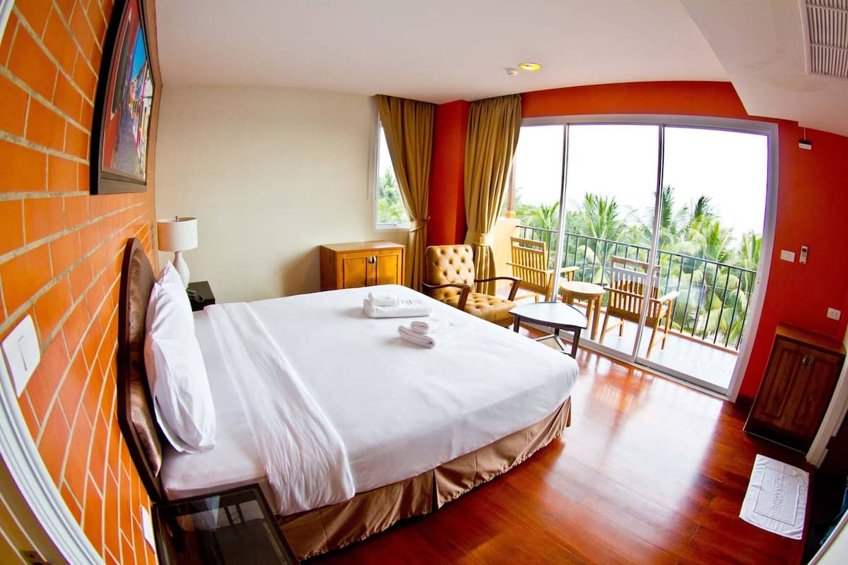 Habitación de hotel con una cama grande, un escritorio, una silla y un balcón con vista a palmeras.