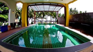 A swimming pool with a tiled edge, surrounded by a covered area with chairs and a fence. - Coasta Bangsaen (Chonburi)