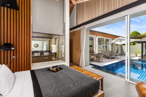 A modern hotel room with a large bed, a wooden slat wall, a view of a swimming pool, and a dining area with outdoor furniture. - Villa Sunpao (Choeng Thale)