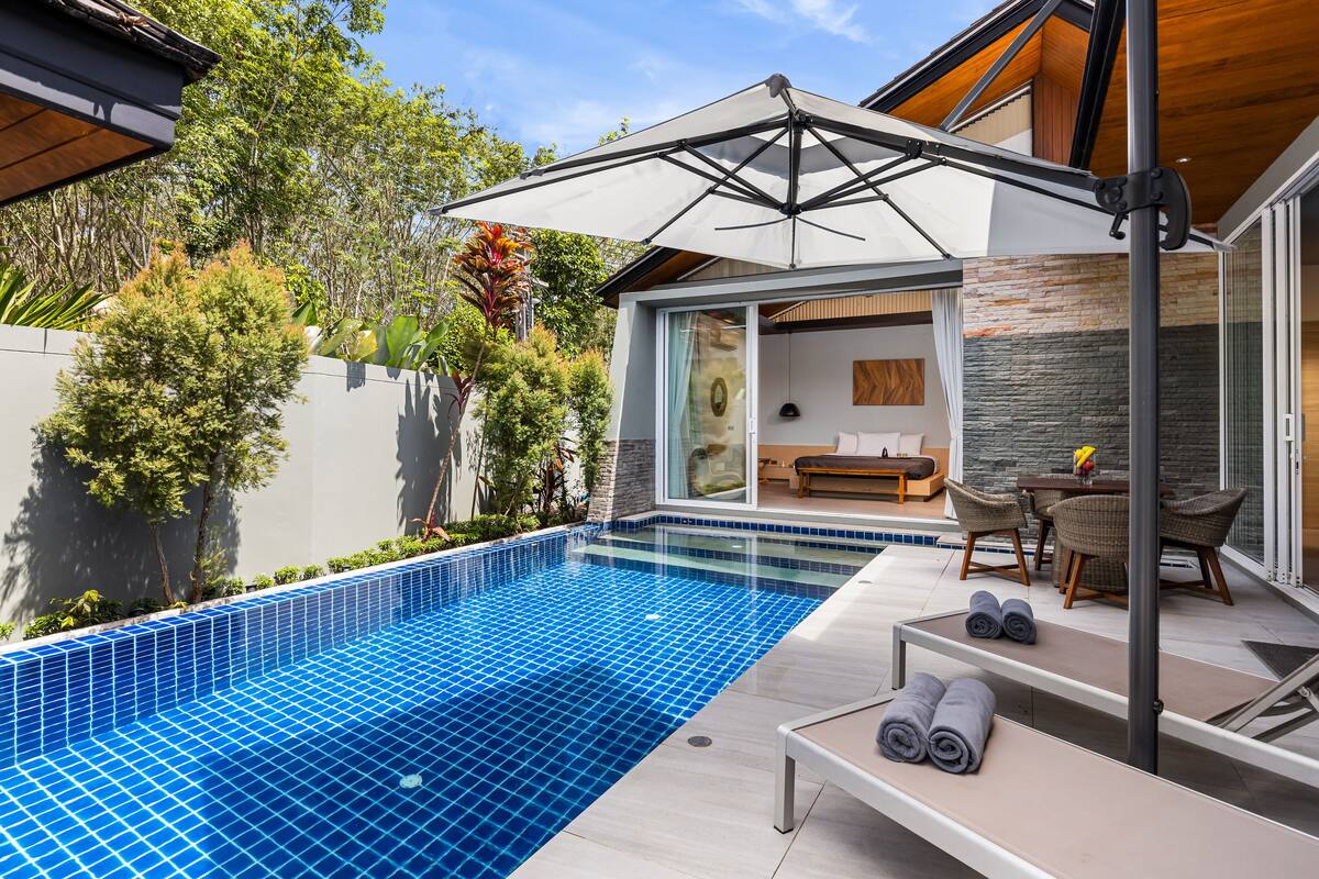 A modern outdoor pool area with a glass-enclosed lounge, a dining set, and a pergola providing shade.