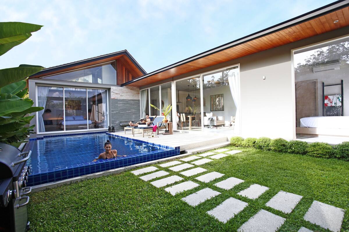 A modern house with a swimming pool, a patio with outdoor furniture, and a well-maintained lawn.