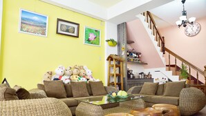 A living room with a sofa, coffee table, and wicker furniture. There are pictures on the wall and a staircase in the background. - Feng's B&B (Hualien City)