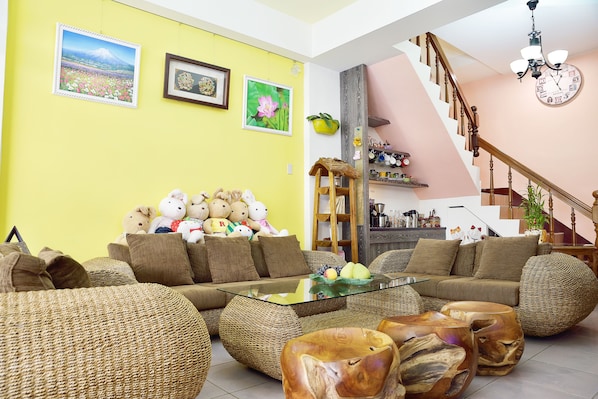 A living room with a sofa, coffee table, and wicker furniture. There are pictures on the wall and a staircase in the background.