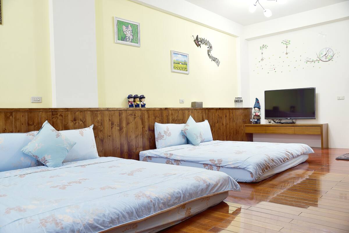 Une chambre d’hôtel avec deux lits, une tête de lit en bois, un téléviseur à écran plat et des éléments de décoration murale, notamment un tableau représentant un paysage et une image de papillon.