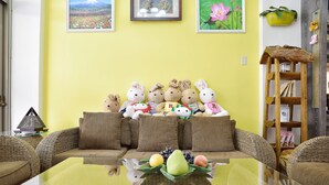 A living room with a yellow wall, wicker furniture, and a glass coffee table with fruit. - Feng's B&B (Hualien City)