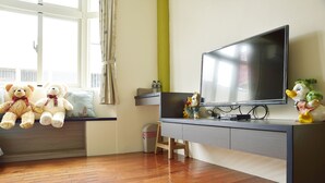 A room with a wooden floor, a TV on a stand, a window with curtains, and two teddy bears on a shelf. - Feng's B&B (Hualien City)