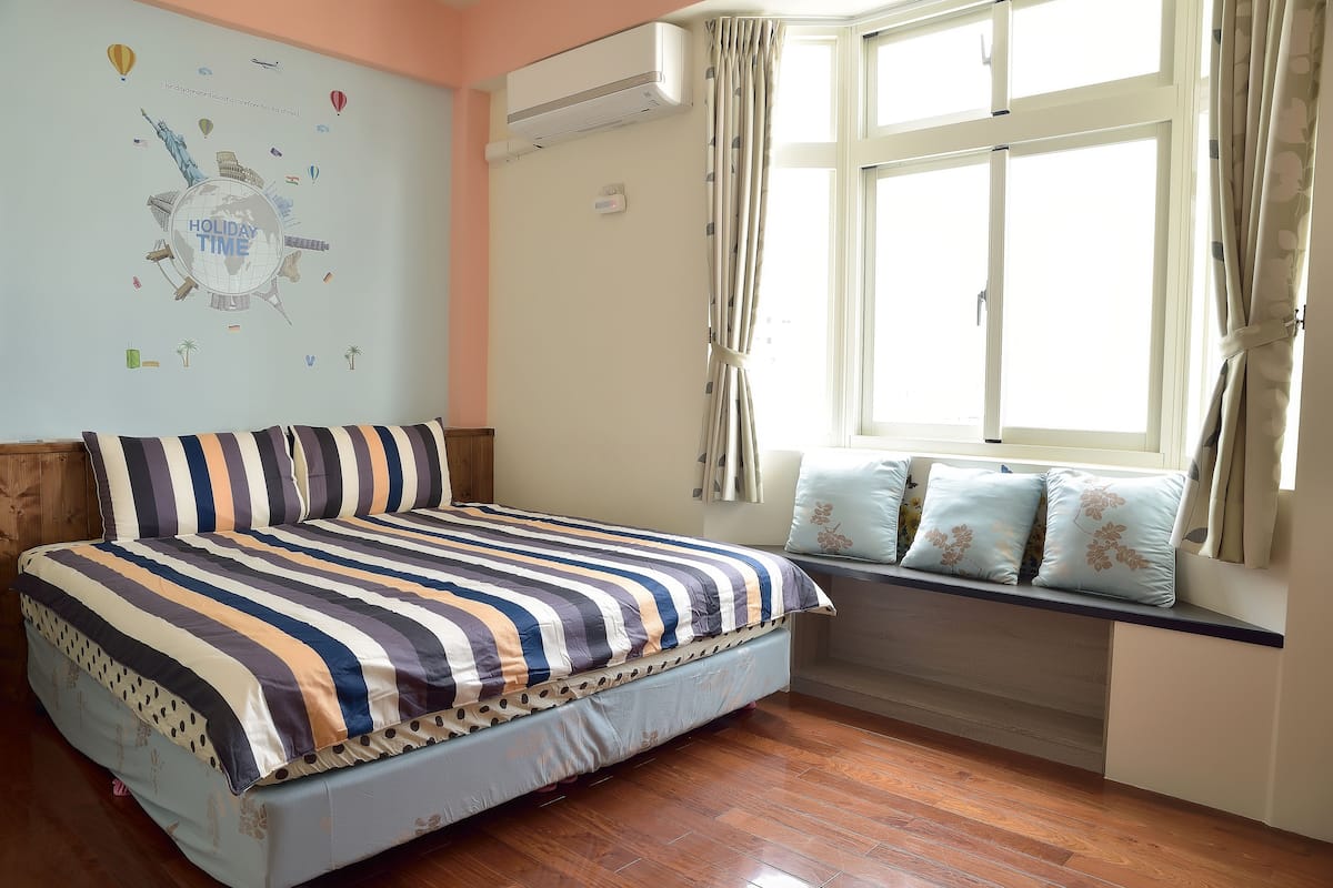 Une chambre à coucher avec un lit, une fenêtre avec des rideaux, un climatiseur fixé au mur et un élément décoratif mural.