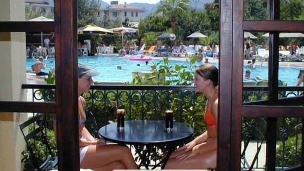 A view of a pool area with lounge chairs and umbrellas, a dining table with chairs, and a building in the background. - Club Turquoise Apartments (Marmaris)