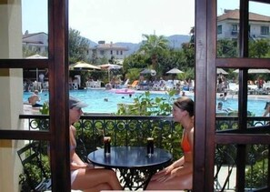 A view of a pool area with lounge chairs and umbrellas, a dining table with chairs, and a building in the background.