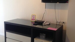 A small office space with a desk, a flat-screen TV mounted on the wall, a telephone, and a small refrigerator. - Similan Mansion (Chonburi)