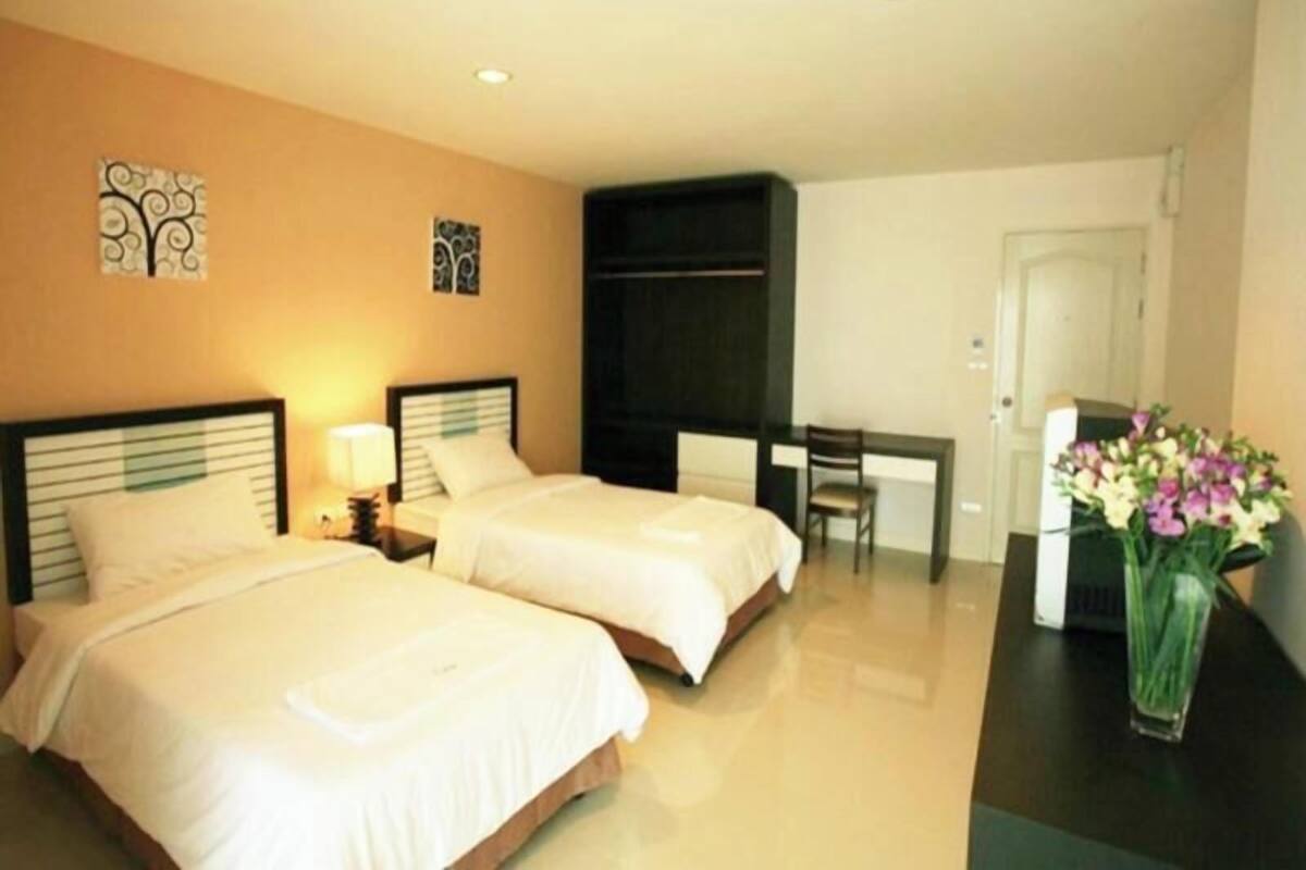 A hotel room with two beds, a desk, a chair, and a vase with flowers.