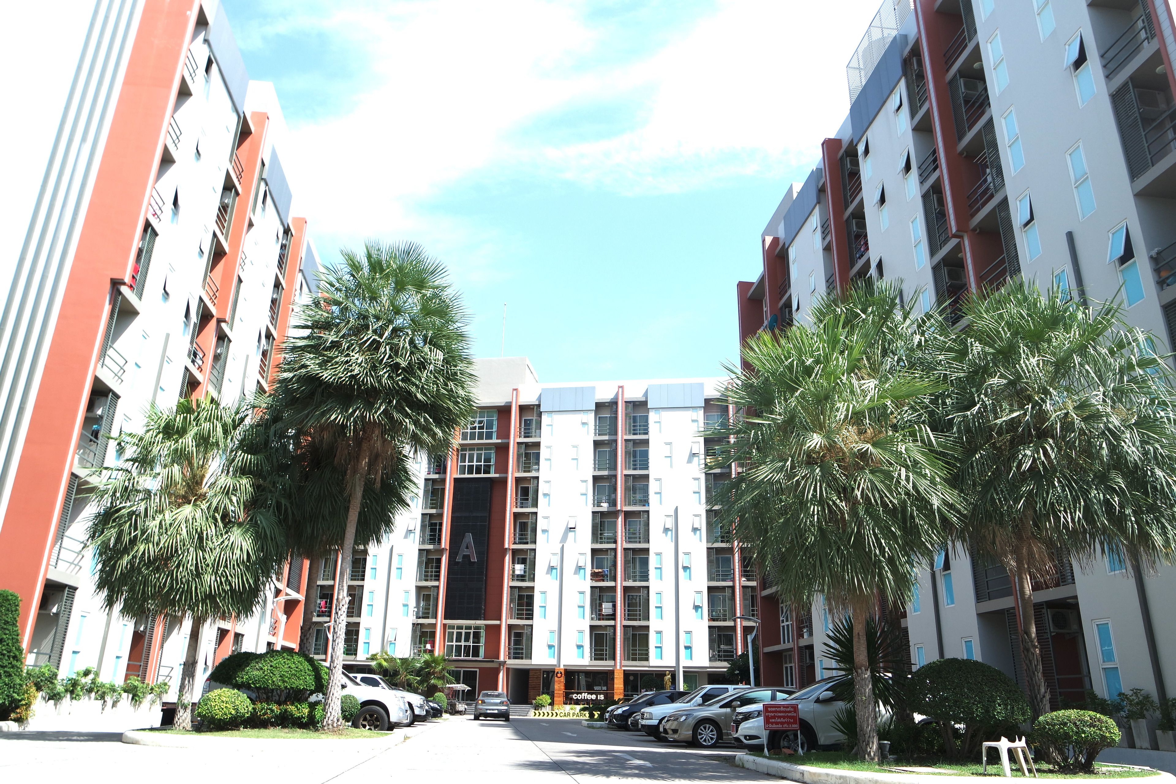 A multi-story residential building with balconies, a coffee shop, and a parking area. - Similan Mansion (Chonburi)