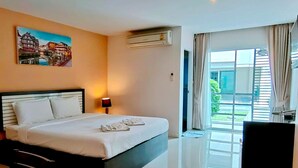 A hotel room with a bed, a desk, a lamp, an air conditioner, a painting, and a large window with curtains. - Similan Mansion (Chonburi)