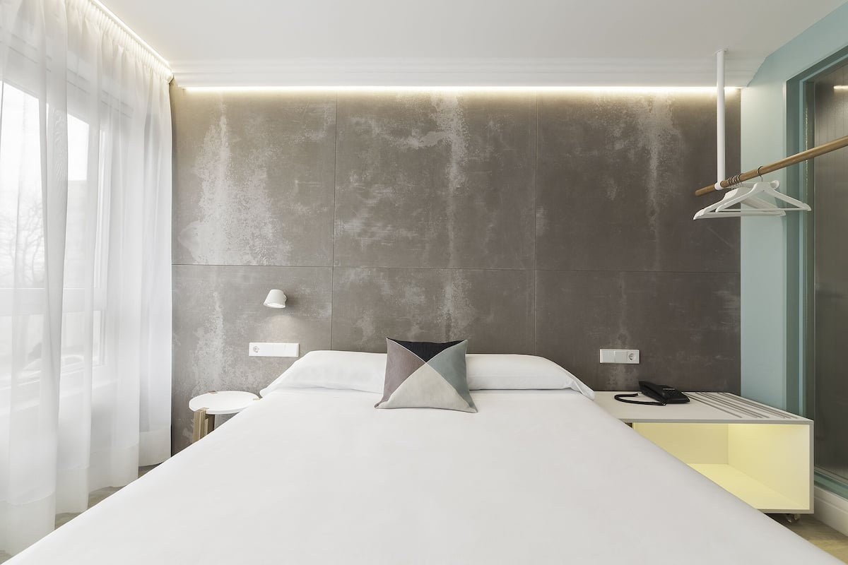 Quarto de hotel moderno com uma cama grande, mesas de cabeceira, uma mesinha e um lustre.