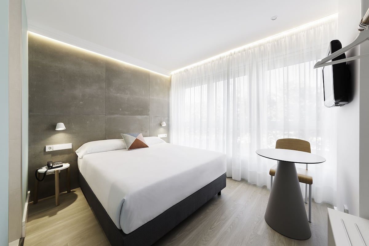 Quarto de hotel moderno com uma cama grande, mesa de cabeceira e uma pequena mesa redonda.