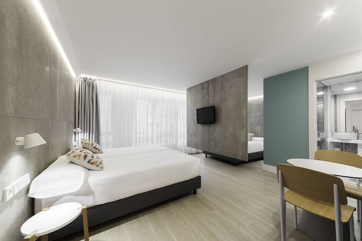 Quarto de hotel moderno com cama, mesas de cabeceira, escrivaninha e banheiro.