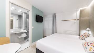 Una habitación de hotel moderna con una cama grande, un televisor montado en la pared, un vestidor y un baño con espejo y lavamanos.