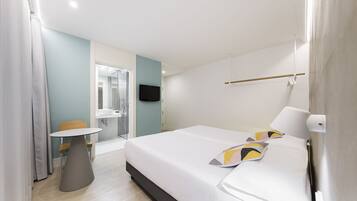 A modern hotel room with a large bed, a bedside table, a chair, a small table, a TV, and a shower area.