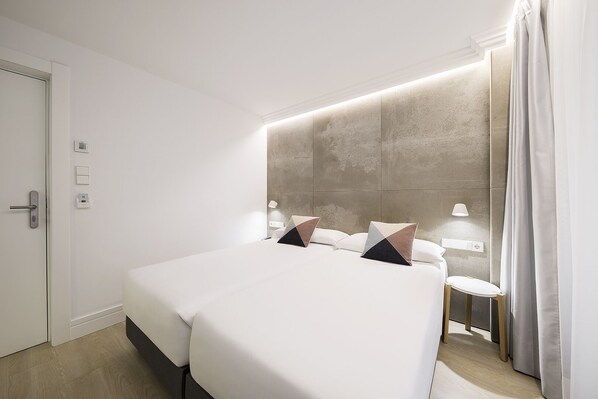 A modern hotel room with a large bed, bedside tables, and a wall-mounted light fixture.