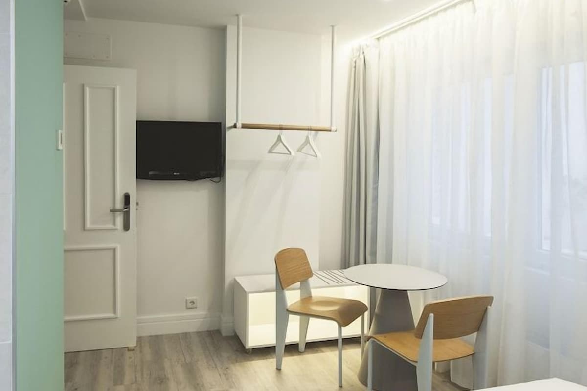 Habitación de hotel con cama, escritorio, dos sillas, televisión y ventana con cortinas.