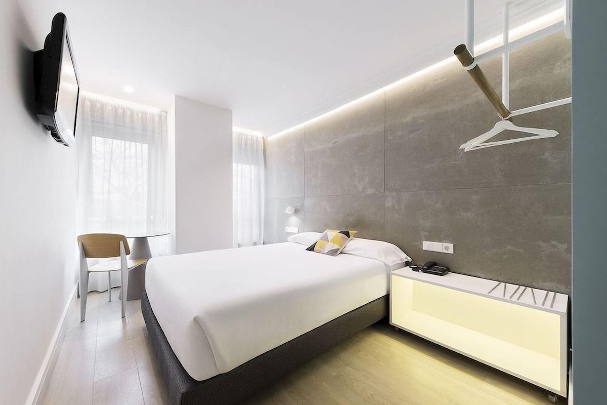 A modern hotel room with a bed, bedside table, and a wall-mounted TV.