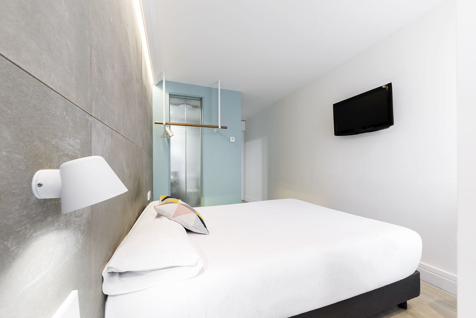 Une chambre d’hôtel moderne équipée d’un lit, d’un téléviseur fixé au mur et d’une lampe également fixée au mur.