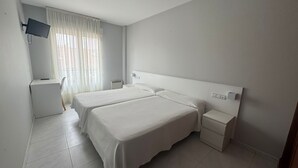 Una habitación de hotel limpia y moderna, con dos camas, un escritorio y un televisor montado en la pared.
